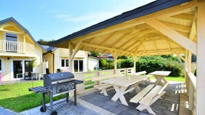 Eine überdachte Terrasse im Freien mit Picknicktischen und einem Grill.