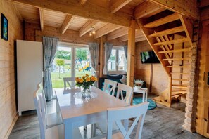 Interior de una cabaña de madera con una mesa de comedor, sillas, un televisor y una escalera.