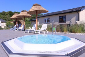 Piscina con sillones de playa y sombrillas de paja.