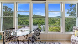A room with a glass table and chairs, large windows with a view of a lake and forest, and a sign above the windows. - Lakeview Penthouse Condo with Sunroom & Amenities (Branson)