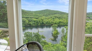 A room with a large window offering a view of a lake surrounded by lush greenery and hills. - Lakeview Penthouse Condo with Sunroom & Amenities (Branson)