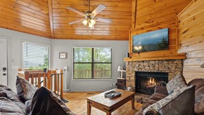 A cozy living room with a fireplace, wooden ceiling, and a stone wall. - Mountain Cabin with Hot Tub, Game Room & BBQ Grill (Gatlinburg)