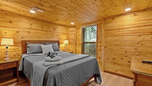 A wooden cabin room with a bed, two bedside lamps, a window, and a wooden cabinet. - Mountain Cabin with Hot Tub, Game Room & BBQ Grill (Gatlinburg)