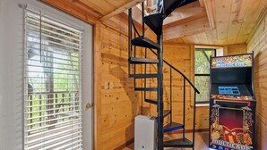 A wooden cabin interior with a spiral staircase, a door with blinds, and a Multicade arcade machine. - Mountain Cabin with Hot Tub, Game Room & BBQ Grill (Gatlinburg)