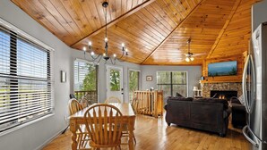 A spacious living area with a wooden ceiling, a dining table with chairs, a sofa, a fireplace, and a television mounted on the wall. - Mountain Cabin with Hot Tub, Game Room & BBQ Grill (Gatlinburg)