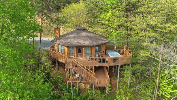A wooden cabin with a deck, hot tub, and outdoor seating area surrounded by trees. - Mountain Cabin with Hot Tub, Game Room & BBQ Grill (Gatlinburg)