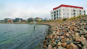 A waterfront hotel with a red roof, multiple balconies, and a rocky shoreline. - Ferienappartement im Ostseeresort Olpenitz (Ostseeresort Olpenitz)