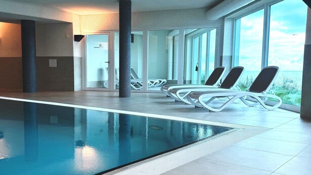 A swimming pool with lounge chairs, a large window, and a modern interior design. - Ferienappartement im Ostseeresort Olpenitz (Ostseeresort Olpenitz)