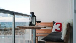 A balcony with a table holding a bottle and two glasses, a wooden bench with a cushion, and a wall-mounted light. - Ferienappartement im Ostseeresort Olpenitz (Ostseeresort Olpenitz)