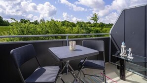 A balcony with a table and two chairs, overlooking a green landscape.