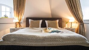 Une chambre avec un plafond haut et incliné, un grand lit recouvert d’une couverture tricotée, deux lampes de chevet et une fenêtre avec des rideaux.