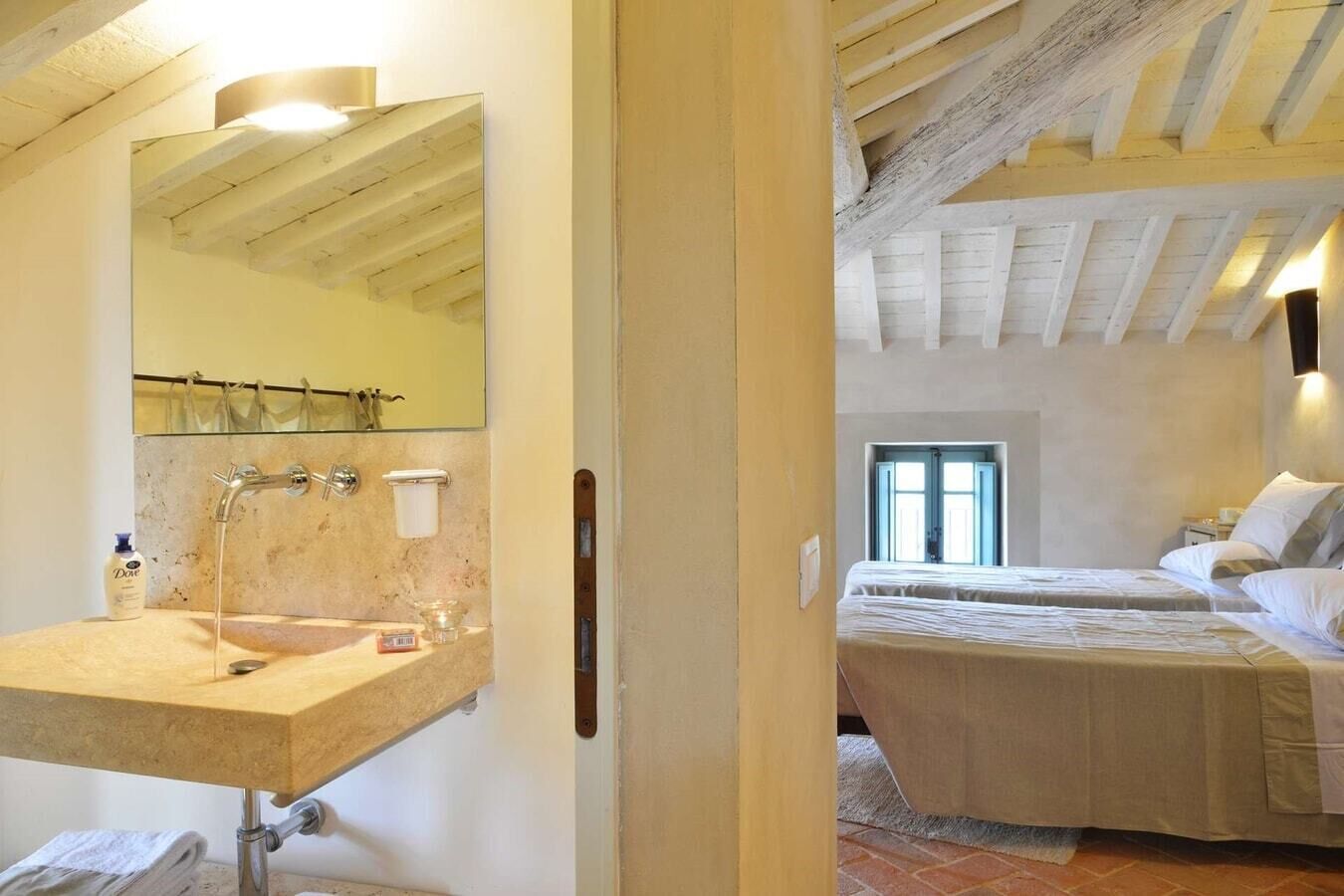 A bedroom with a bed, a window, and a bathroom with a sink and mirror.