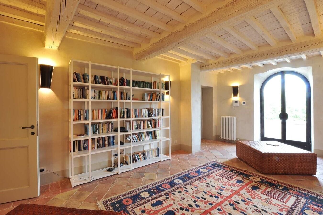 Une pièce spacieuse avec une grande bibliothèque, un tapis à motifs et une vue dégagée sur l’extérieur grâce à une grande fenêtre en arc de cercle.