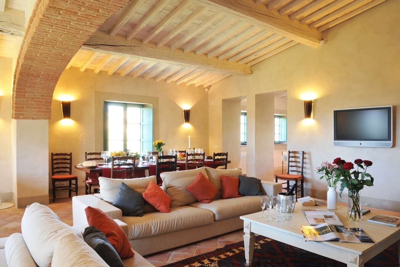 A spacious living area with a high ceiling, a dining area with a brick arch, and a flat-screen TV mounted on the wall.