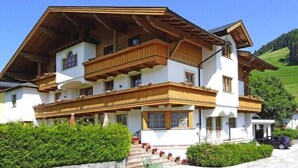 Un immeuble à plusieurs étages, doté de balcons en bois et d’un toit en pente, entouré de verdure.