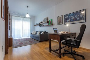 A modern living room with a sofa, a desk with a laptop, and a chair. There are shelves with books and decorative items on the wall. - Casa Torricelli in zona Crocetta by Wonderful Italy (Turin)