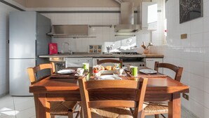 A modern kitchen with white cabinets, a stainless steel range hood, and a dining area with a wooden table and chairs. - Casa Torricelli in zona Crocetta by Wonderful Italy (Turin)