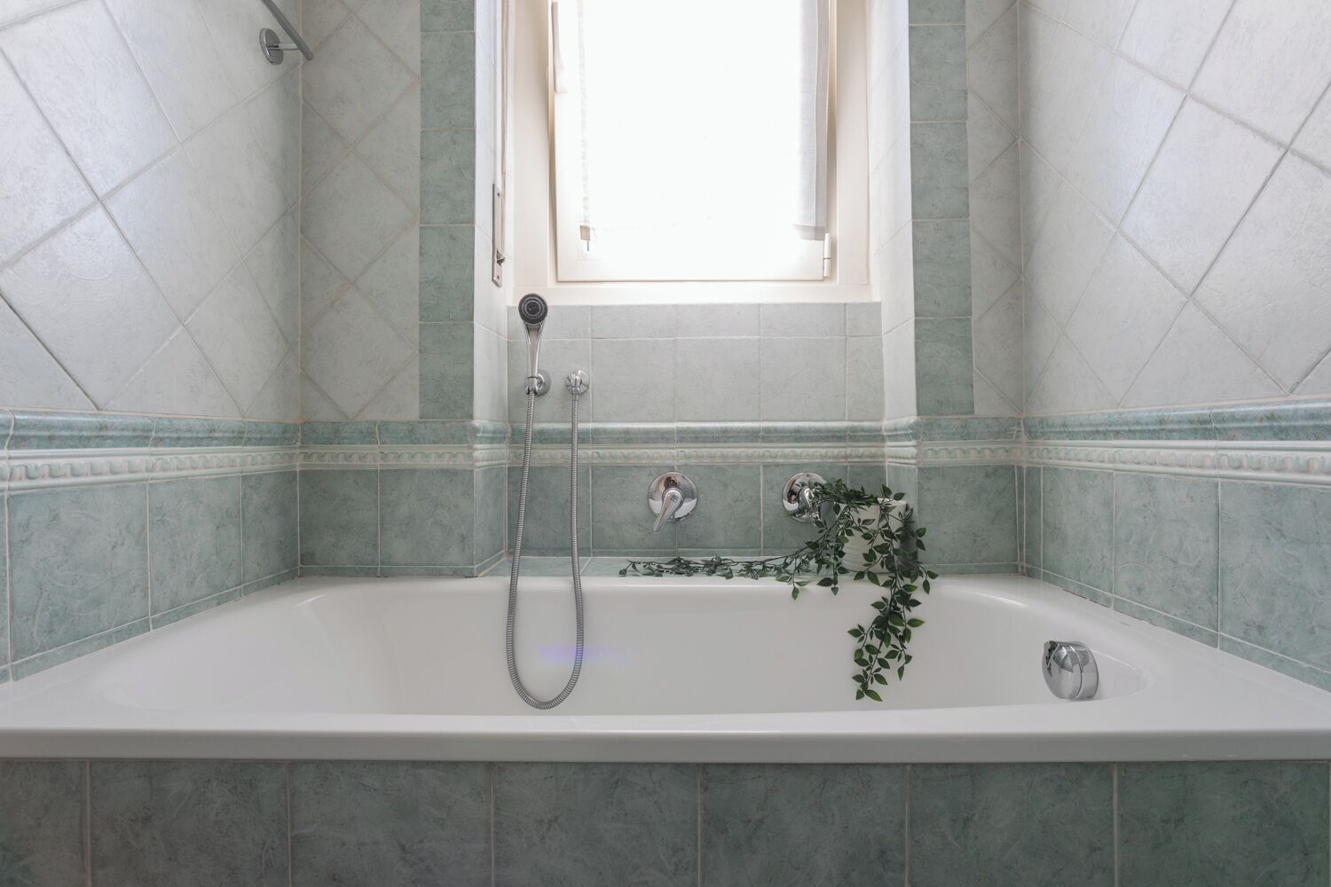 A bathroom with a bathtub, a window, and green-tiled walls.