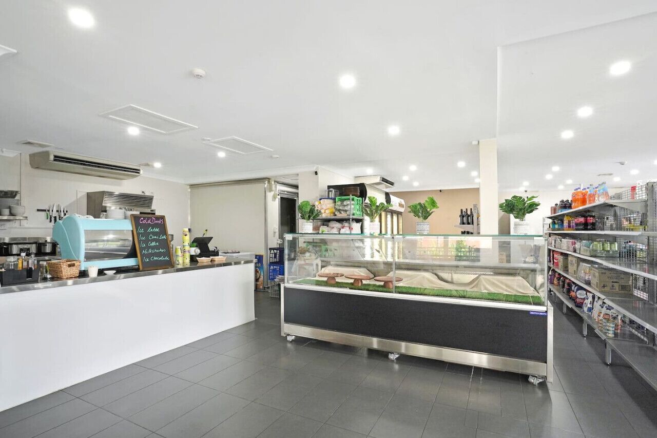 A modern cafe interior with a counter, a display case, and shelves stocked with beverages.