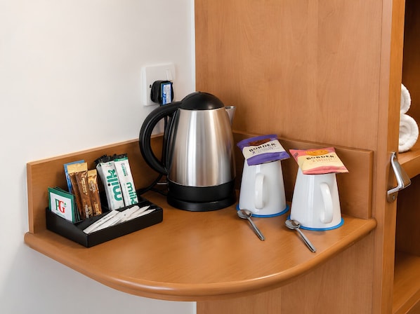 Una pequeña kitchenette con cafetera, hervidor de agua, sobre de café instantáneo y azúcar.