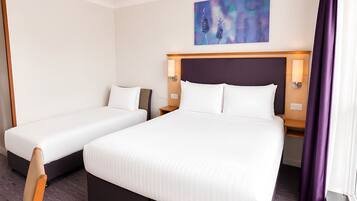 Habitación de hotel con dos camas individuales y una cama doble, un cuadro en la pared y una cortina morada.