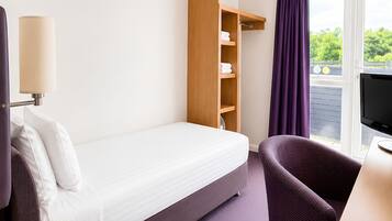 A hotel room with a bed, a wooden wardrobe, a television, and a window with curtains.