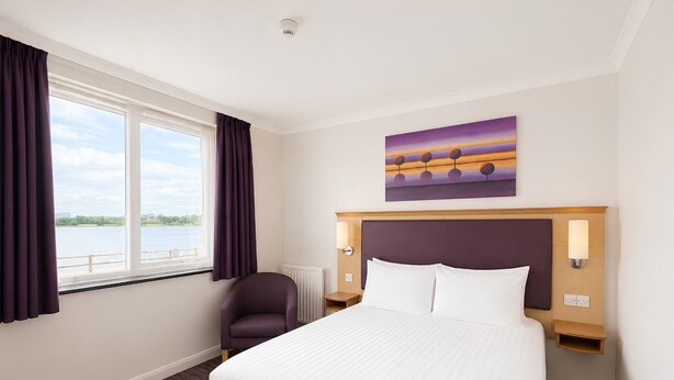 Ein Hotelzimmer mit einem großen Bett, einem Sessel, einem Gemälde und Blick ins Freie.