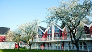 A multi-story building with a red and white color scheme, featuring balconies and a white fence.