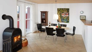 A dining area with a black wood-burning stove, a round table with chairs, a cabinet, and a painting on the wall.