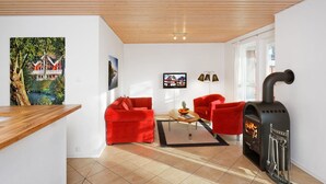 A living room with a fireplace, two red sofas, a coffee table, and a TV on the wall.