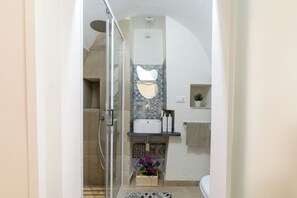 A compact bathroom with a glass shower enclosure, a white sink with a geometric backsplash, and a small shelf with toiletries. - Stairway with Jacuzzi by Wonderful Italy (Ostuni)