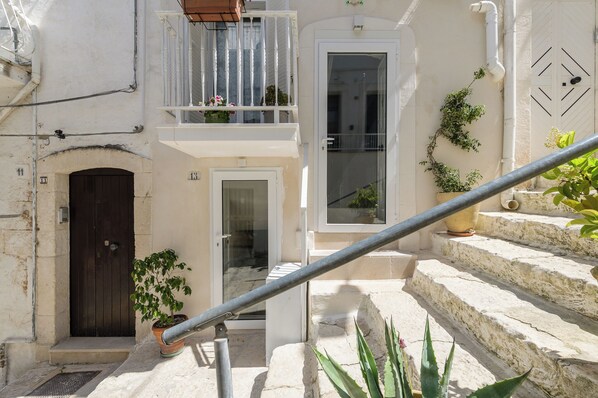 Un patio estrecho con una escalera de piedra, una puerta y un balcón con macetas.