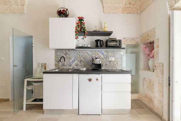 A compact kitchen with white cabinets, a built-in oven, a coffee maker, and a toaster.