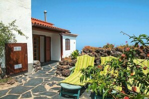 A stone-tiled patio with a chair and a table, a small building with a red-tiled roof, and a garden with plants and a yellow chair. - Apartment in El Tanque with bubble bath (El Tanque)