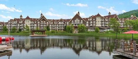 A hotel with a large lake in front, featuring a gazebo and a dock with boats.