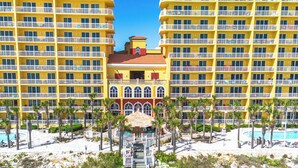 A multi-story hotel with balconies, a central courtyard with a pool, and a beach area.