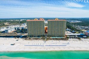A high-rise hotel with multiple floors, a beach in the foreground, and a clear view of the ocean.