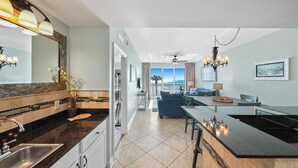 A modern kitchen with a central island, a dining area with a blue sofa, and a view of the ocean through large windows.