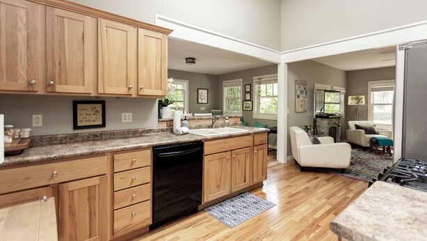 A spacious kitchen with wooden cabinets, a dishwasher, and a large island. There is a living area with a sofa and a rug.