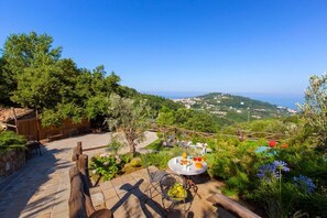 A patio with a table set for a meal, surrounded by lush greenery and a scenic view of the sea and hills. - VILLA ALESSANDRA , SANTA AGATA DEI DUE GOLFI (Sant'Agata Sui Due Golfi)