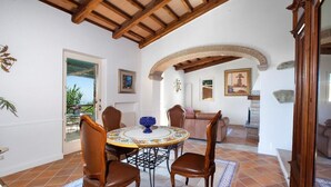 A dining area with a round table, four chairs, and a decorative bowl. An archway leads to a living room with a sofa and a painting. - VILLA ALESSANDRA , SANTA AGATA DEI DUE GOLFI (Sant'Agata Sui Due Golfi)