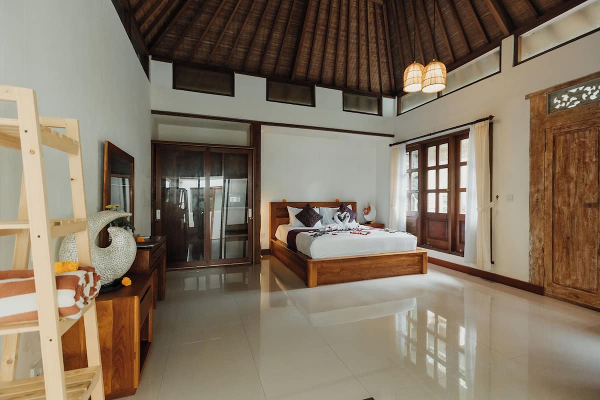 A spacious bedroom with a large bed, wooden furniture, and a high ceiling with exposed beams.