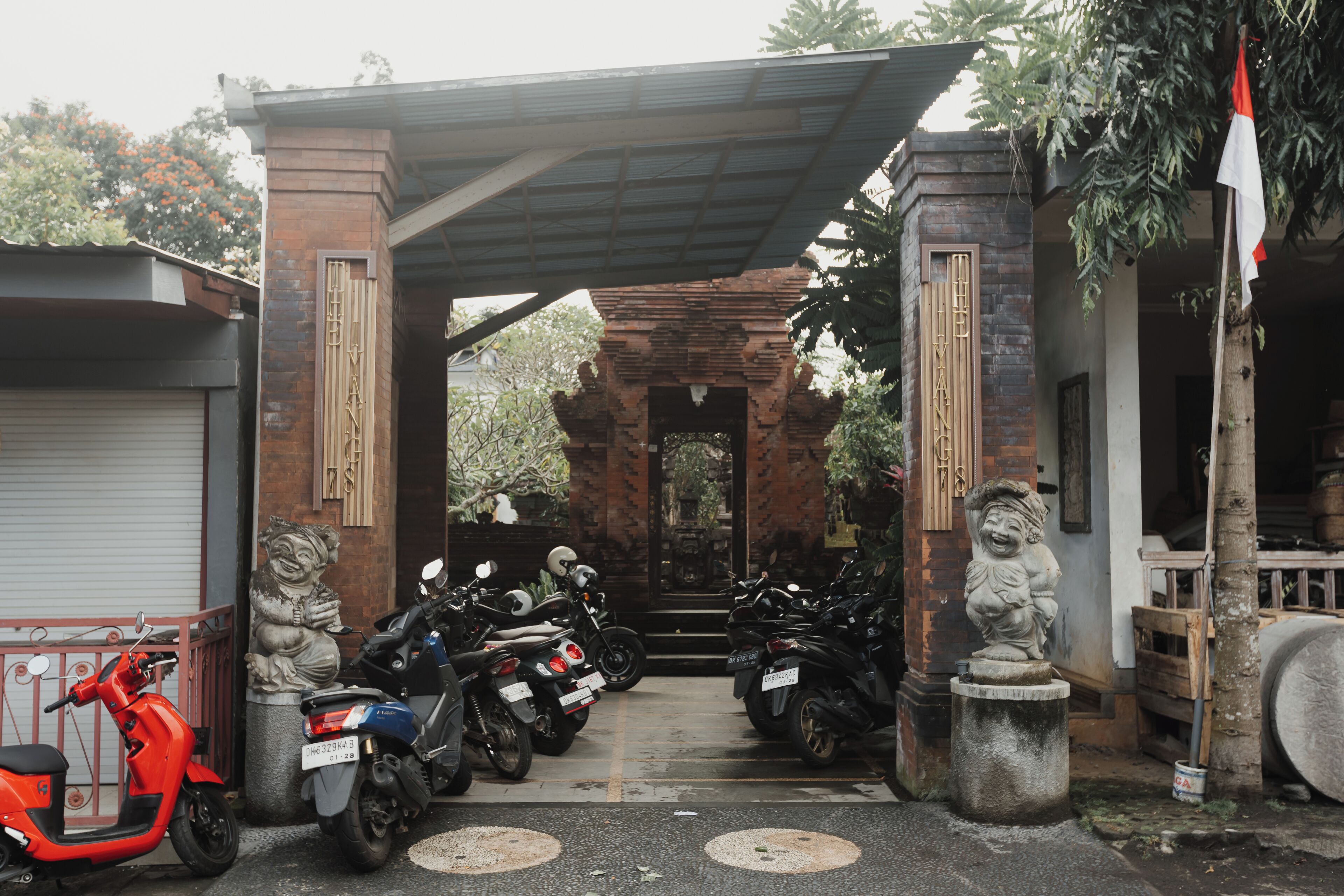 A covered entrance with a traditional archway, a statue, and a row of parked motorcycles.