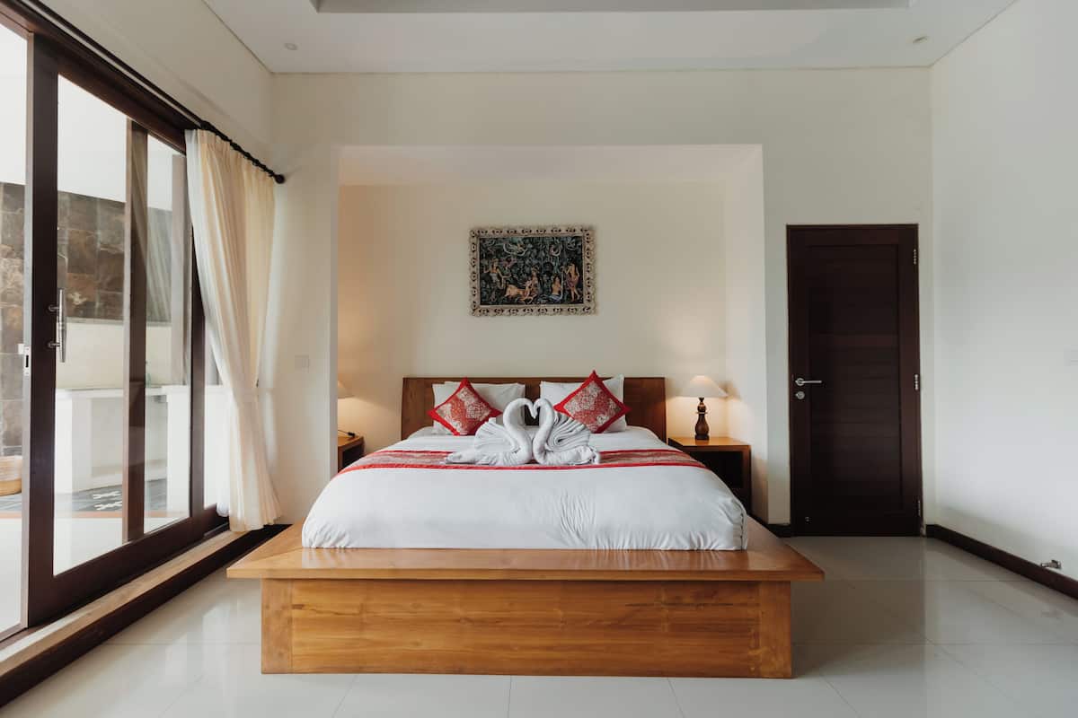 A large bed with a wooden frame, a headboard, and a bedside table with a lamp.