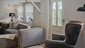 Een moderne woonkamer met een bank, fauteuil en lamp. Er is een raam met gordijnen en een deur met een deurklink.
