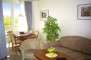 Een woonkamer met een bank, een eettafel met stoelen, een plant in een pot en ingelijste foto's aan de muur.