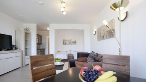 A modern living room with a dining table, a fruit bowl, and a sofa. - Ferienwohnung in Cuxhaven-Duhnen (Cuxhaven)
