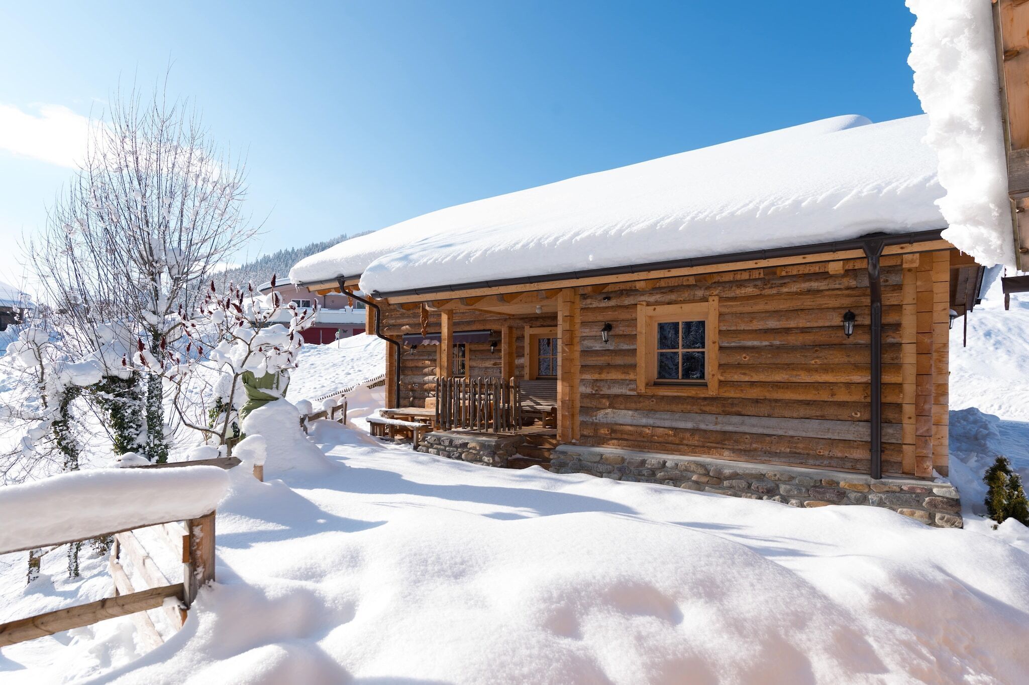 Une cabane en bois, avec un toit enneigé et des fondations en pierre.