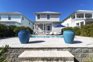 A two-story house with a swimming pool, two large blue planters, and a covered patio area.