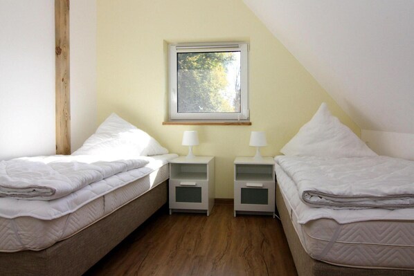 Une petite pièce bien éclairée, avec deux lits simples, une fenêtre et un plancher en bois.